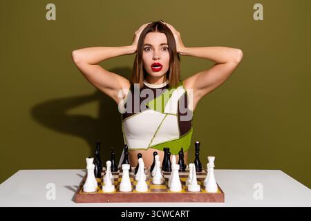 Besorgte Frau, die beim Schachspiel vor grünem Hintergrund einen überraschenden Ausdruck zeigt und einen angespannten Moment erlebt Stockfoto
