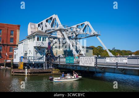 Ein kleines Boot navigiert durch das Wasser des Mystic River in Mystic, CT, in New England, von der Mystic River Bascule Bridge aus gesehen, während eines wunderschönen fa Stockfoto