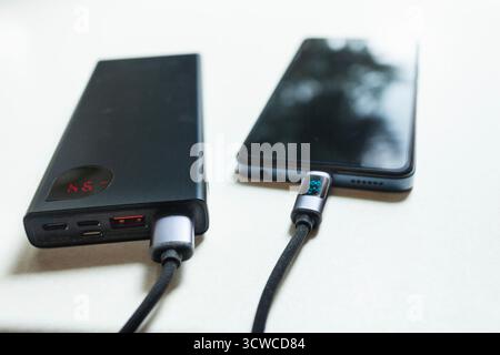 Nahaufnahme eines Smartphones, das über ein USB-Kabel von einer Powerbank aufgeladen wird Stockfoto