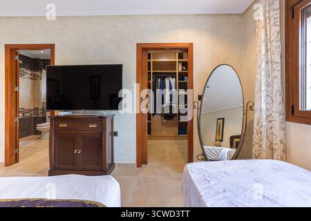 Modernes Schlafzimmer mit großem Flachbild-TV auf Holzständer, einem sichtbaren begehbaren Kleiderschrank mit organisierter Kleideraufbewahrung und einem kompletten Schrank Stockfoto