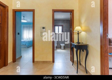 Gut beleuchteter Flur in einem modernen Haus mit beigefarbenem Fliesenboden und weichen gelben Wänden. Der Flur bietet Zugang zu einem Schlafzimmer mit Stockfoto