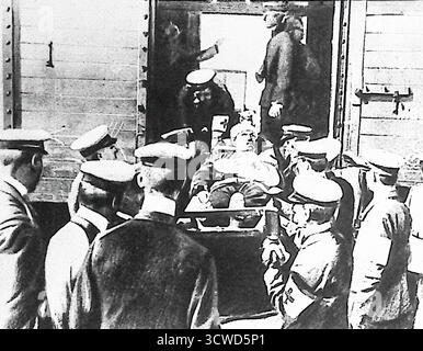 Dieses Schwarzweiß-Bild aus dem Le Miroir vom Oktober 1914 zeigt verwundete Soldaten, die in München ankommen. Ein Team des Roten Kreuzes wird gezeigt, wie er die Bahren eines Zugwagens entlädt, beobachtet von deutschen Offizieren. Obwohl die Zahl der Opfer oft verborgen wurde, zeigten Fotos von Konvois die hohe Zahl des Krieges. Das Bild veranschaulicht sowohl die menschlichen Kosten der Kämpfe als auch die Rolle der medizinischen Dienste bei der Bewältigung von Kriegsverletzungen. Stockfoto