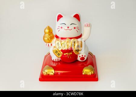 Maneki-neko. Japanische und chinesische Glückskatze auf weißem Hintergrund mit Kopierraum. Die Katze hält eine Münze, auf der gut geschrieben ist Stockfoto