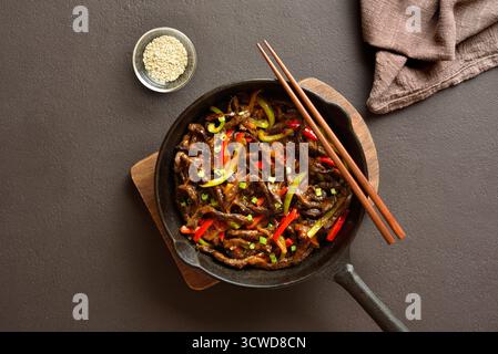 Chinesische Pfanne mit frittiertem, dünn in Streifen geschnittenem Rindfleisch und Paprika auf dunkelbraunem Hintergrund. Draufsicht, flach Stockfoto