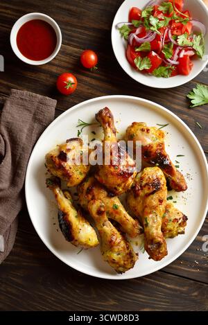 Gebratene Hähnchenkeulen mit Sauce und Salat aus frischem Gemüse auf braunem Holztisch. Draufsicht, flach Stockfoto