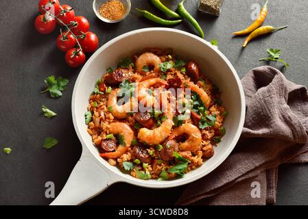 Kreolischer Jambalaya mit Garnelen, geräucherten Würstchen und Gemüse in einer hellen Pfanne auf dunklem Hintergrund. Nahansicht Stockfoto