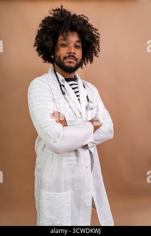 Junger schwarzer Arzt, der einen Labormantel und ein Stethoskop mit überkreuzten Armen trägt Stockfoto