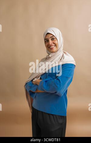 Lächelnde Frau, die einen Hijab trägt und selbstbewusst mit überkreuzten Armen posiert Stockfoto