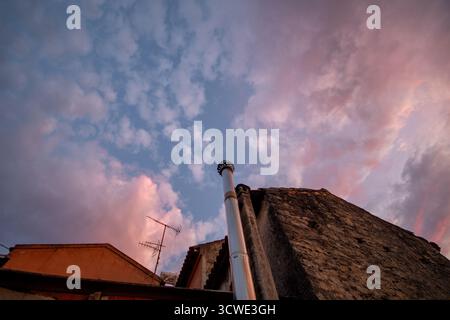 Eine Perspektive aus einem niedrigen Winkel fängt ein traditionelles Steingebäude und einen Kamin vor einem traumhaften Himmel mit flauschigen rosa Wolken ein, die durch Flecken von blu treiben Stockfoto