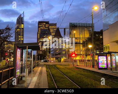 Urbane Nachtszene mit Straßenbahnschienen, modernen Gebäuden und Straßenbahnhaltestelle in der belebten Stadt Haag, Niederlande Stockfoto