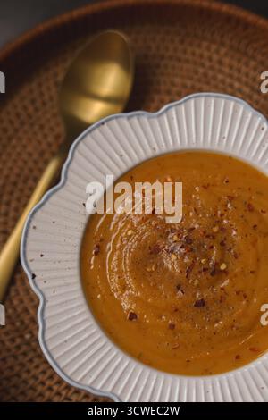 Cremige Butternusskürbis- und Kürbissuppe in einer eleganten Schüssel, garniert mit Chili-Flocken und schwarzem Pfeffer, perfekte Komfortgerichte Stockfoto
