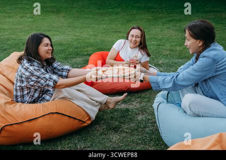 Freunde, die sich auf bunten Sitzsäcken im Freien entspannen und Essen und Getränke in zwangloser geselliger Atmosphäre mit einem kleinen Hund teilen. Frau informell Stockfoto