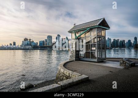 Ein einzigartiges Gebäude am Wasser bietet einen Blick auf die Skyline der Stadt, während die Sonne über dem Hafen und den Bergen untergeht. Stockfoto