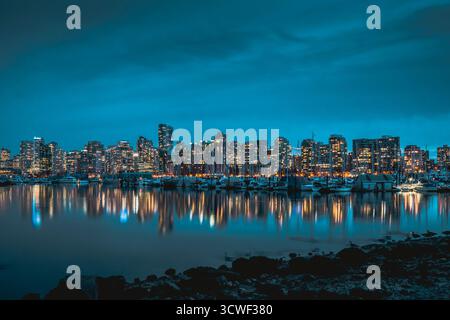 Helle Stadtlichter leuchten auf einer ruhigen Wasseroberfläche und erzeugen eine atemberaubende Reflexion. Die Aussicht fängt eine lebhafte urbane Szene in einer Küstenstadt ein Stockfoto