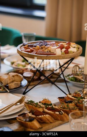 Luxuriöse Wurstplatte mit Schinken, Käse, Brotbacken und Salaten auf einem wunderschön gedeckten Esstisch, der an Feiern und Feiern erinnert Stockfoto