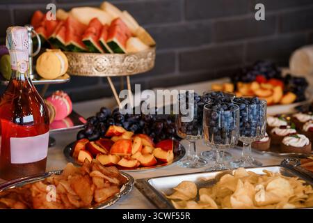 Eine wunderschön gestaltete Obstplatte mit Champagner, Gebäck und verschiedenen Snacks wird auf einer dunklen Arbeitsplatte präsentiert und präsentiert eine elegante CA Stockfoto