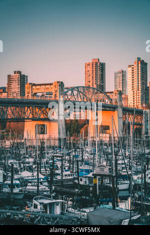 Boote legen in einem Jachthafen mit einer Skyline im Hintergrund an, während ein farbenfroher Sonnenuntergang das pulsierende urbane Leben veranschaulicht. Stockfoto