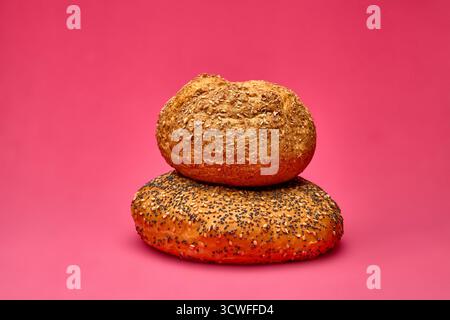 Zwei frisch gebackene Brötchen in verschiedenen Formen und Körnern auf rosafarbenem Hintergrund. Eine kreative Bäckerei-Komposition, ideal für Design und Stockfoto