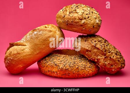 Künstlerische Komposition von drei verschiedenen Brötchen auf rosafarbenem Hintergrund, fotografiert im Studio-Licht. Konzeptuelles Stillleben geeignet für Bäckereiwerbung Stockfoto