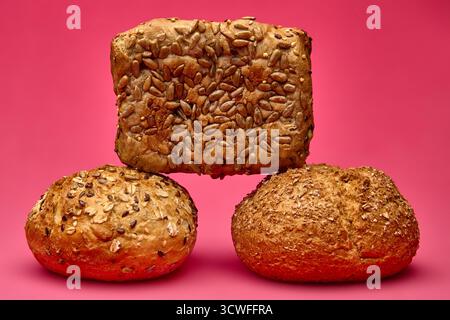 Quadratische mehrkörnige Brotscheibe, gestapelt über zwei runde Brötchen auf rosa Hintergrund. Konzeptionelle kreative Komposition für Bäckerei, gesunde Lebensmittel oder Diät visuell Stockfoto