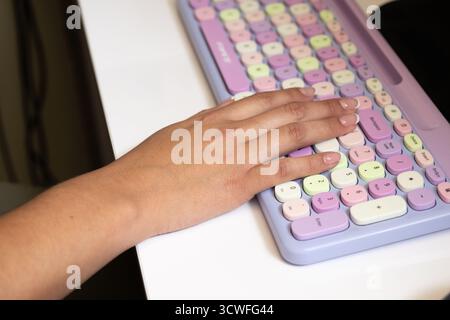 Weibliche Handtasten auf der farbenfrohen Bürotastatur, die Daten für das Unternehmen eingibt. Stockfoto