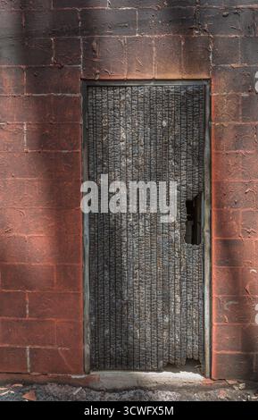 Tür aus verkohltem Holz in einer roten Ziegelwand, die erhebliche Brandschäden aufweist. Stockfoto