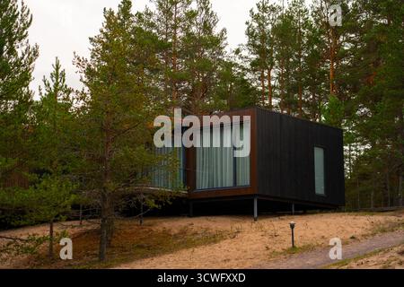 Altai, Russland - 13. Mai 2024: Eine elegante, schwarz-braune, moderne Kabine mit großen Fenstern liegt auf einem Sandhang, umgeben von hohen Kiefern Stockfoto