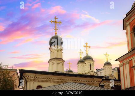 Die Kuppeln und goldenen Kreuze einer Moskauer orthodoxen Kirche heben sich deutlich von einem Himmel ab, der mit rosa und violetten Tönen bemalt ist Stockfoto