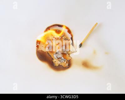 Die Abbildung zeigt, dass das Papier kreisförmig verbrannt wird, wobei dunkelbraune Brandspuren auf dem weißen Papier durch eine Übereinstimmung hinterlassen werden. Stockfoto
