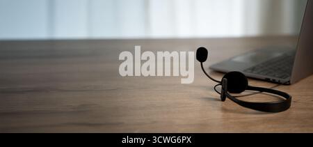 Minimales Headset mit Mikrofon auf Holzschreibtisch in der Nähe des Laptops großer Kopierraum in ruhigem Home Office für Kommunikationsunterstützung Callcenter für Kundenservice Stockfoto
