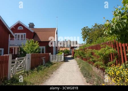 Die Dorfstraße in Sandhamn im Stockholmer Archipel führt mit einem schmalen Schotterweg zwischen traditionellen schwedischen roten Holzhäusern Stockfoto