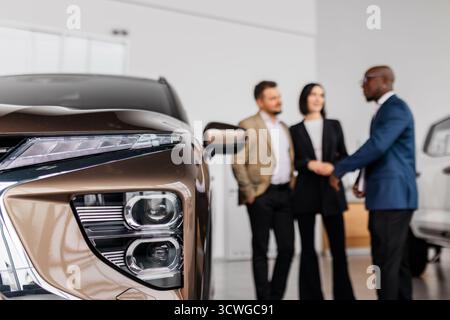 In einem zeitgenössischen Ausstellungsraum diskutierten verschiedene Gruppen über Fahrzeugmerkmale, wobei ein stilvolles Fahrzeug im Mittelpunkt stand, das eine einladende und bekennende Atmosphäre schafft Stockfoto