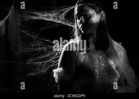 Kunstfoto einer jungen Frau in Spinnennetz auf schwarzem Hintergrund. Schwarzweißfoto Stockfoto