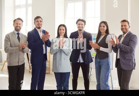 Gruppe glücklicher, selbstbewusster Geschäftsleute, die in die Kamera schauen, lächeln und applaudieren. Stockfoto