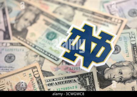 KIEW, UKRAINE - 23. FEBRUAR 2025 Notre Dame Fighting Irish Basketball Team Badge liegt auf einer großen Menge von US-Dollar-Scheinen Stockfoto