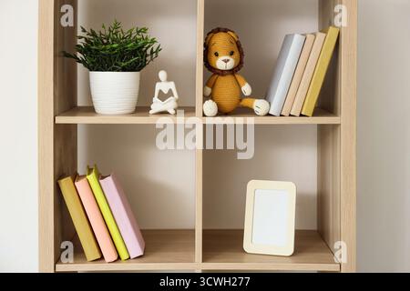Holzregal mit Büchern, Spielzeug und Zimmerpflanzen in der Nähe der weißen Wand im Kinderzimmer Stockfoto