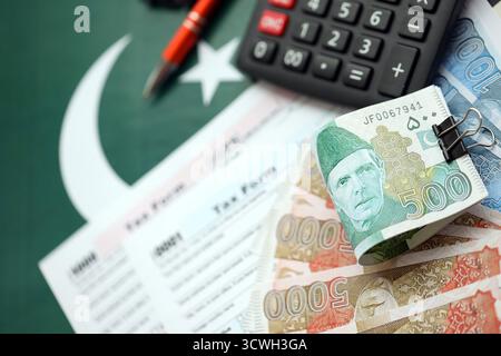 Pakistanische Rupien Banknoten mit Taschenrechner und Steuerformular. Die aktuellen pakistanischen Echtgeldrechnungen und Steuerpauschalen aus nächster Nähe. Das Konzept der Steuerzahlung und Buchhaltung in Pakistan Stockfoto
