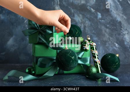 Weibliche Hand mit Weihnachtskugeln und Geschenkboxen auf blauem Grunge-Hintergrund Stockfoto