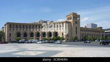 Langgezogenes Steingebäude mit Bögen, vor denen Autos geparkt sind, unter klarem Himmel, Außenministerium, Platz der Republik, Jerewan, Yer Stockfoto