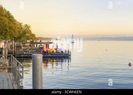 Ein Fluss mit bunten Figuren und ein Segelboot auf dem ruhigen See bei Sonnenaufgang, Ueberlingen, Bodensee, Deutschland Stockfoto