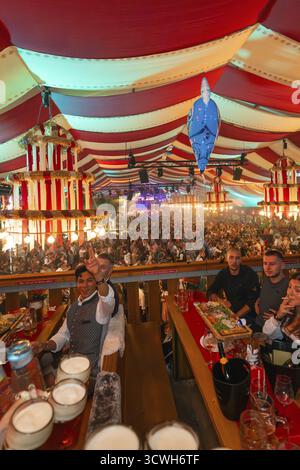 Menschen feiern an einem langen Tisch in einem bunten gestreiften Festzelt, Cannstatter Wasen Volksfest, Stuttgart, Deutschland Stockfoto