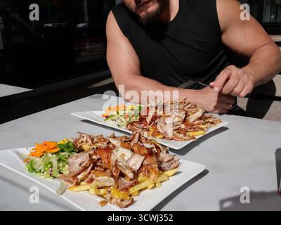 Zwei Teller gegrilltes Shawarma/Gyros-Fleisch mit Pommes Frites und Salat auf einem weißen Tisch im Freien, während eine Person mit einem Fo beginnt Stockfoto