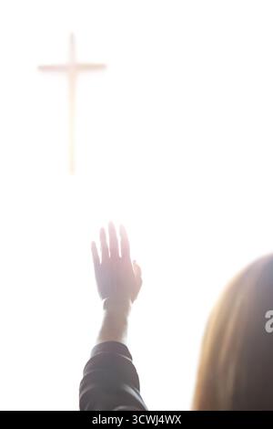 Eine christliche Frau betet und betet mit erhobenen Händen zum Heiligen Kreuz Jesu Christi. Stockfoto