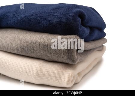 Eine Gruppe warmer Pullover auf weißem Hintergrund. Stapel gefalteter Pullover auf weißem Hintergrund. Stockfoto