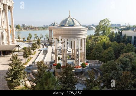 Majestätischer Blick auf den Navruz-Palast in Duschanbe, Tadschikistan, mit großen Säulen, Kuppelpavillons und einer malerischen Seenlandschaft unter einem klaren blauen Stockfoto