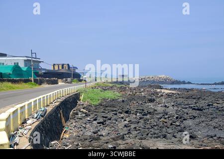 In der Nähe von Dongbok folgt eine niedrige Küstenstraße schwarzen Basaltsteinen zu Betontetrapoden an einem Wellenbrecher, mit verstreuten Trümmern entlang der Mauer und ruhiger W Stockfoto