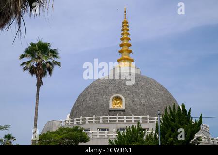 Die Buddha Sharira Stupa für den Frieden und die Vereinigung der Welt erhebt sich mit einer grauen Kuppeltrommel und einem goldenen Turm, umgeben von weißen Brüstungen und Bäumen Stockfoto