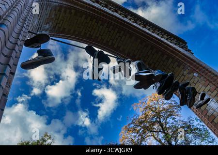 Alte Turnschuhe hängen an einem Draht unter einem Ziegelbogen mit blauem Herbsthimmel und Wolken im Hintergrund Stockfoto