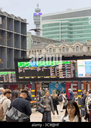 Reisende checken die Abfahrtstafeln am Bahnhof London Euston, mit dem BT Tower im Hintergrund. Stockfoto
