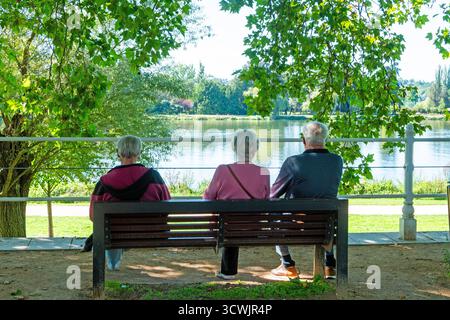 Vichy. Drei ältere Menschen sitzen auf einer Bank und blicken auf den Fluss Allier, während ein junges Paar Erinnerungen in der Nähe festhält. Allier. Auvergne . Frankreich Stockfoto